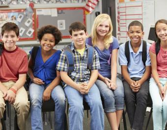 Six students with backpacks sitting on wall